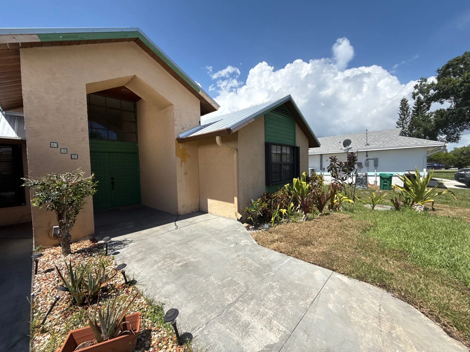 Exterior Painting in Port Saint Lucie, Florida. Single-storey stucco house with green entry door, green fascia and metal roof, with landscaped beds and driveway.