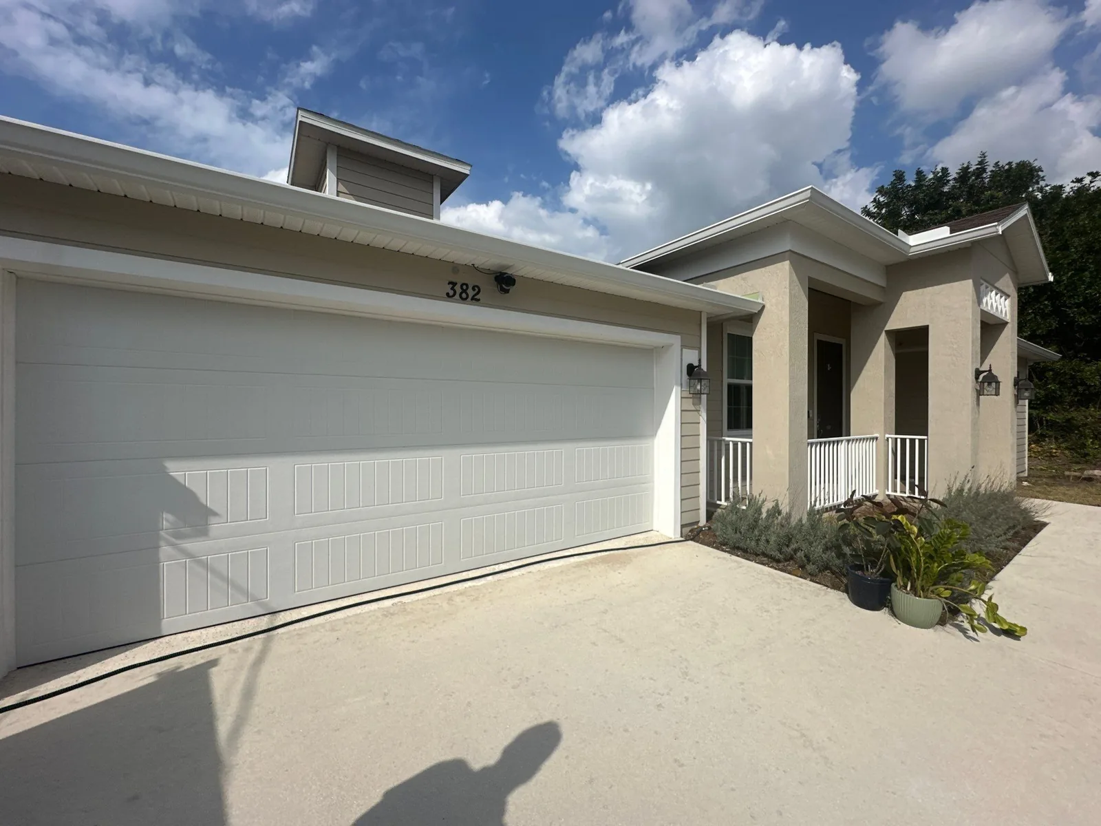 Exterior Painting in Port Saint Lucie, Florida. Single-storey stucco home exterior with white garage door, white trim and covered front porch.