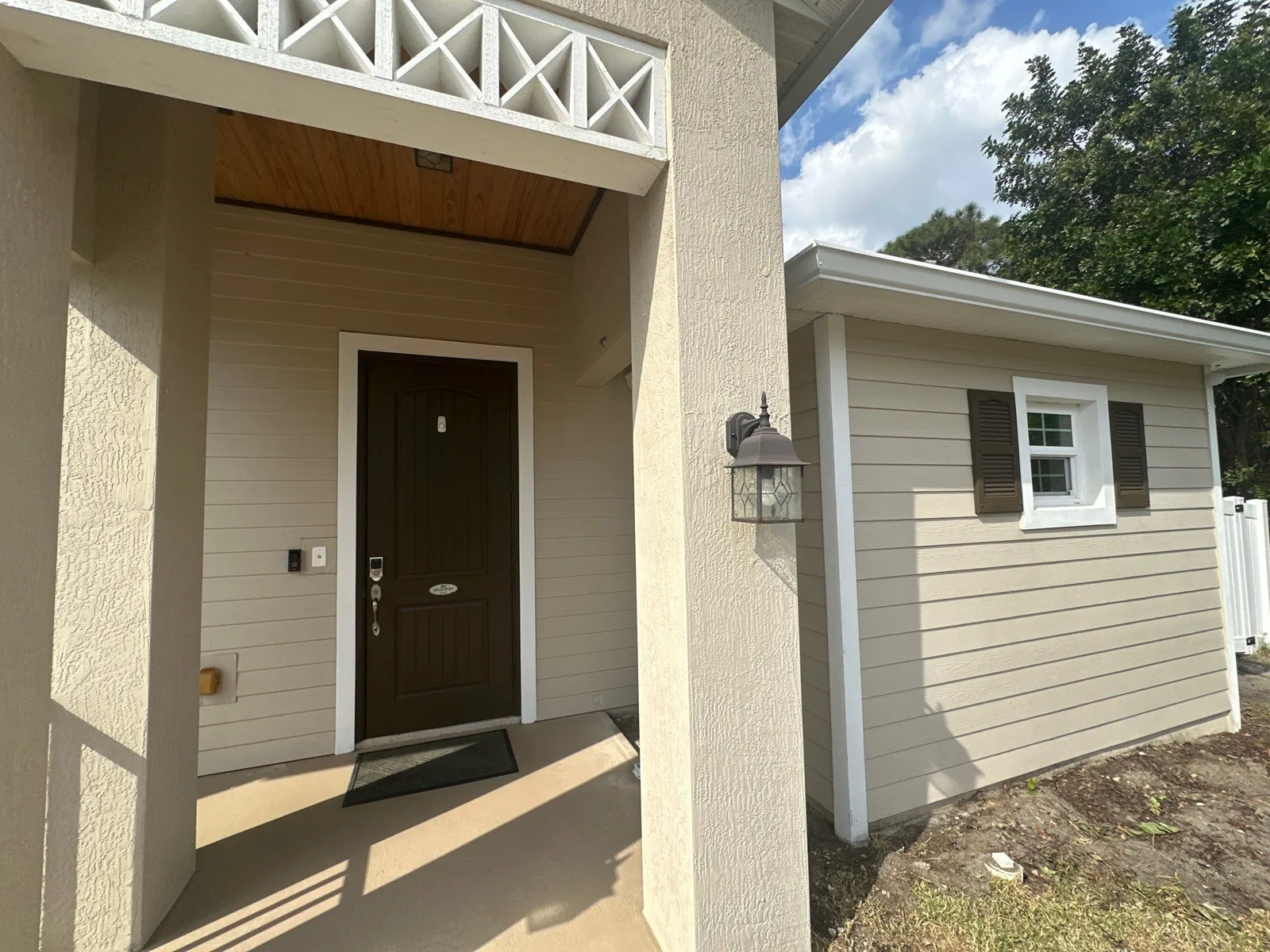 Exterior Painting in Port Saint Lucie, Florida. Front entry with dark brown door, painted lap siding, white trim and wall lantern.