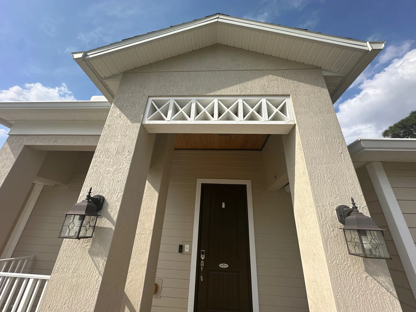 Exterior Painting in Port Saint Lucie, Florida. Front gable entry of a stucco home with white cross-brace trim detail and two wall lanterns.