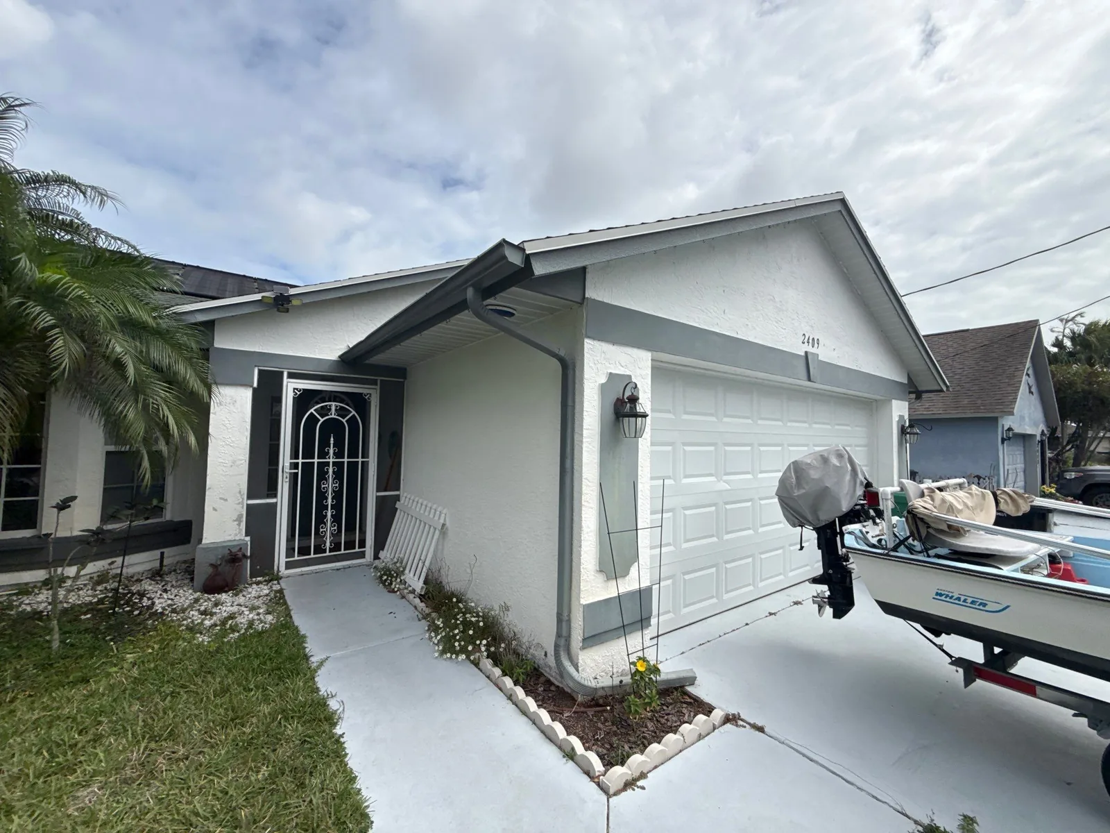 Exterior Painting in Port Saint Lucie, Florida. Front elevation of a single-storey white stucco house with white trim, attached two-car garage, decorative security door and a concrete walkway.