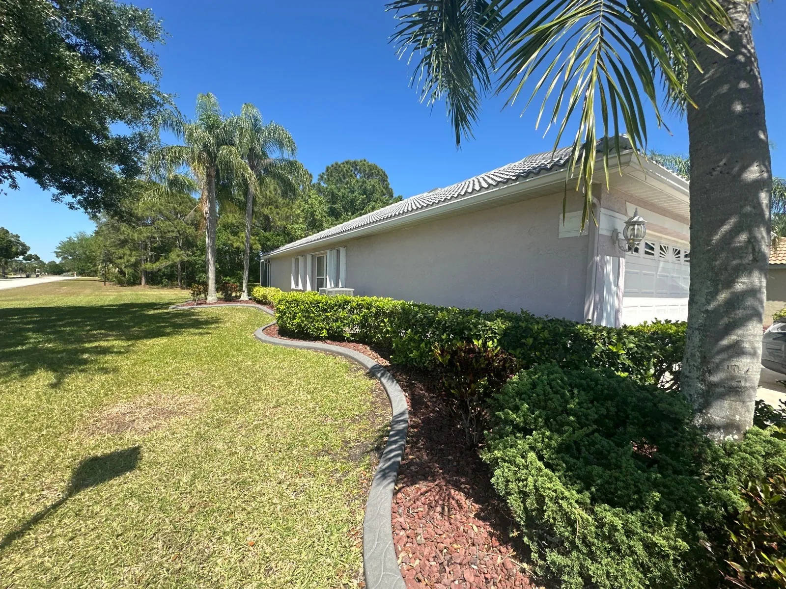 Exterior Painting in Port Saint Lucie, Florida. Side elevation of a single-storey stucco home with tile roof, trimmed hedges and lawn.