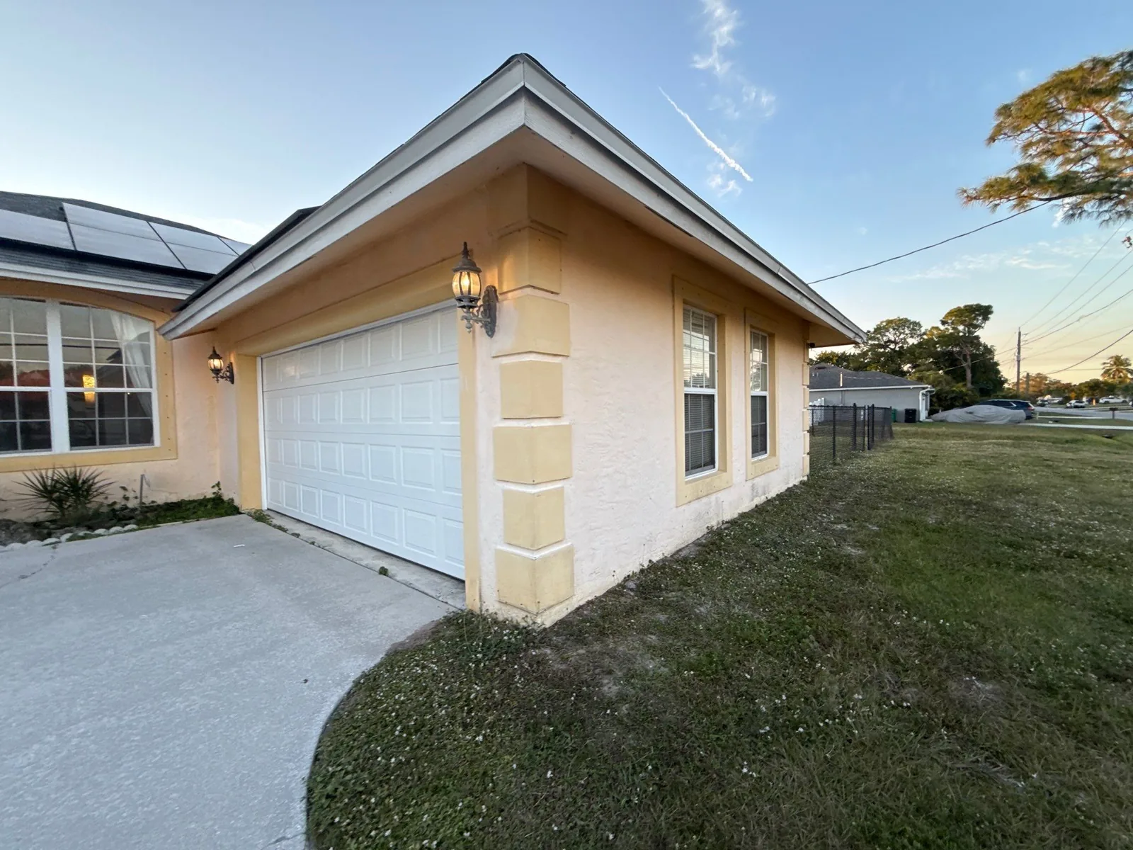 Exterior Painting in Port Saint Lucie, Florida. Angled view of a cream stucco house exterior with white garage door, quoin corner detail and lawn.