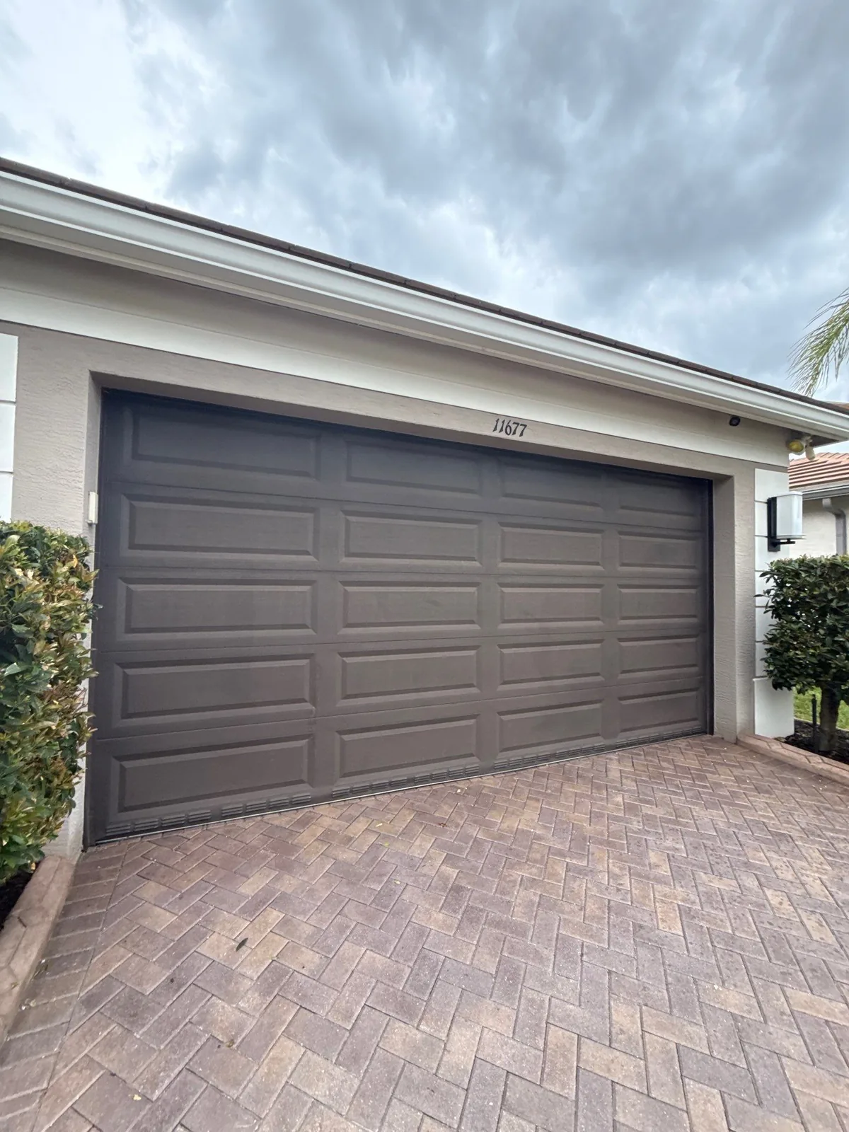 Exterior Painting in Port Saint Lucie, Florida. Two-car garage door painted dark brown on a stucco house with off-white fascia and a herringbone paver driveway.