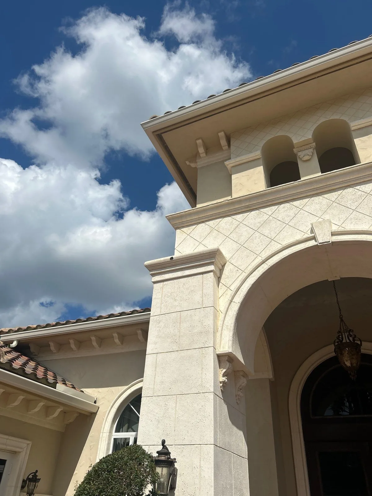 Exterior Painting in Port Saint Lucie, Florida. Upward view of a stucco home entry tower with an arched portico, corbels and tile roof against blue sky.