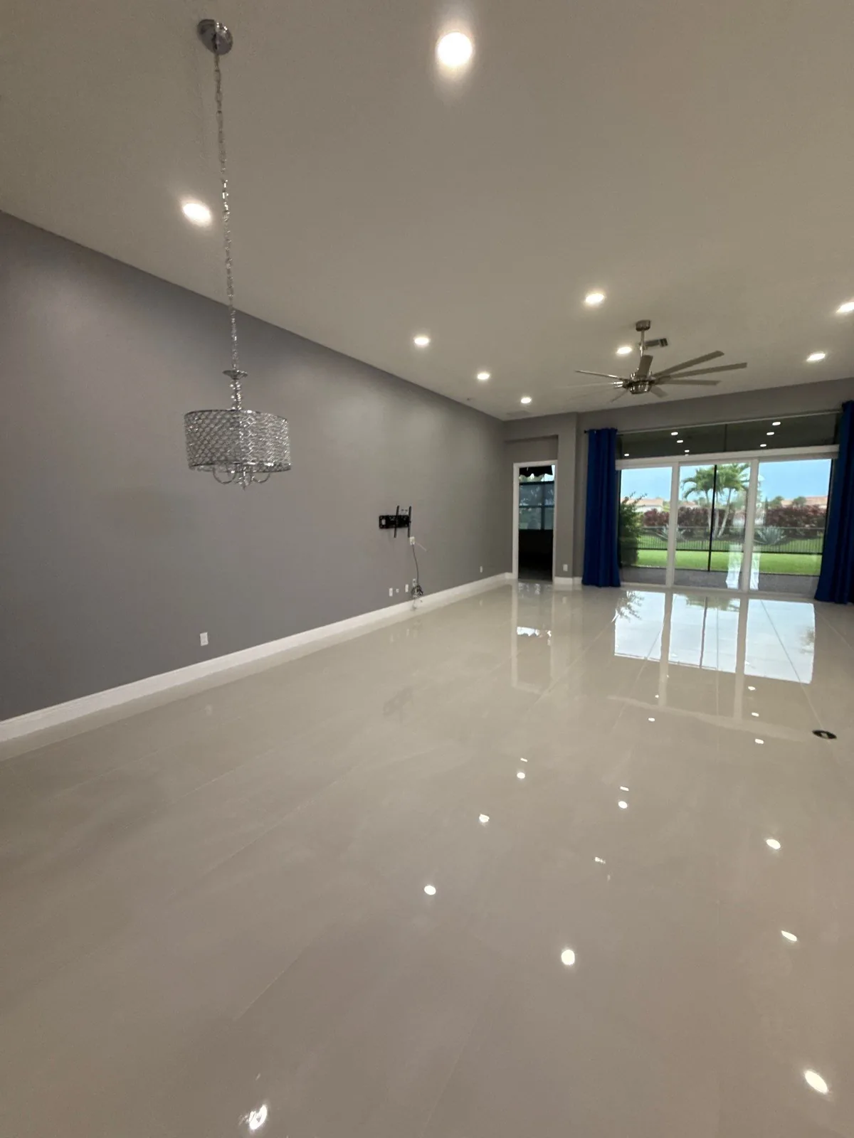 Interior Painting in Port Saint Lucie, Florida. Large empty living area with grey accent wall, white ceiling, ceiling fan and sliding glass doors to a lawn.