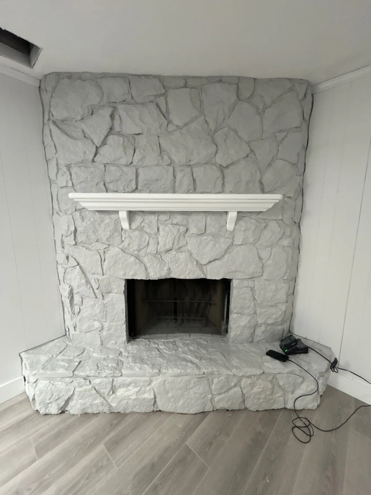 Interior Painting in Port Saint Lucie, Florida. Stone fireplace and hearth painted white with a white mantel shelf, in an empty room with wood-look flooring.