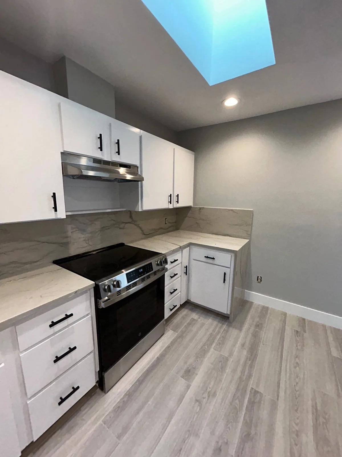 Interior Painting in Port Saint Lucie, Florida. Kitchen with white shaker cabinets, gray painted walls, stone-look counter and backsplash, range and skylight.