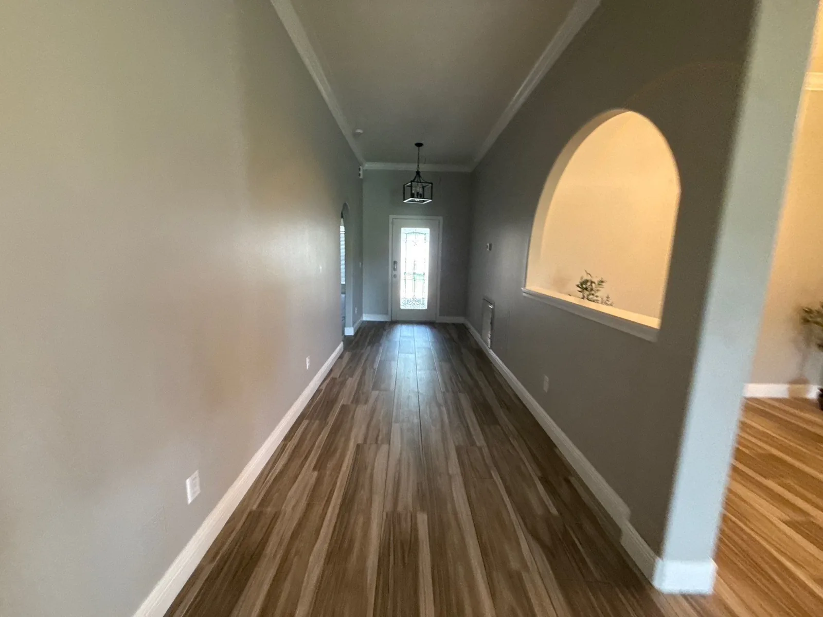 Interior Painting in Port Saint Lucie, Florida. Empty entry hallway with grey walls, white crown moulding and baseboards, arched wall niche and wood-look plank flooring.