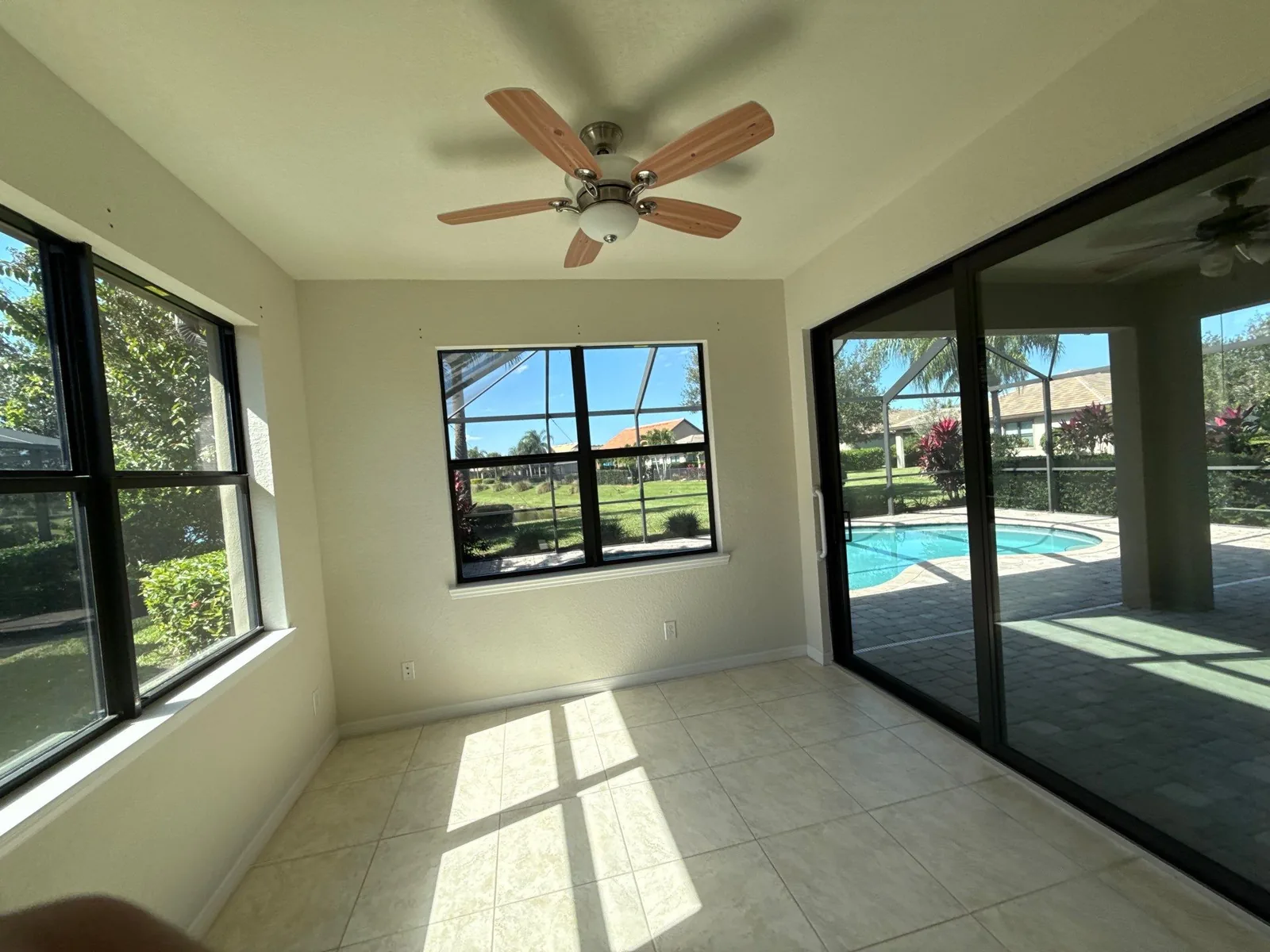 Interior Painting in Port Saint Lucie, Florida. Empty room with off-white painted walls, ceiling fan, tile floor and sliding doors onto a pool deck.