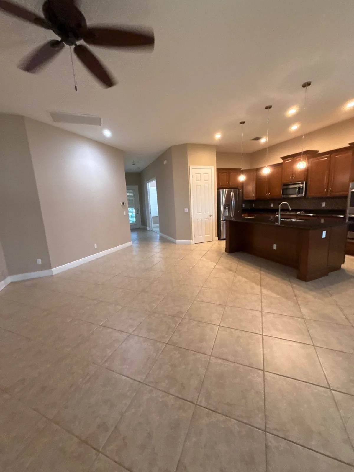 Interior Painting in Port Saint Lucie, Florida. Empty open-plan living area and kitchen with light walls, white baseboards, dark wood cabinets and tile floor.