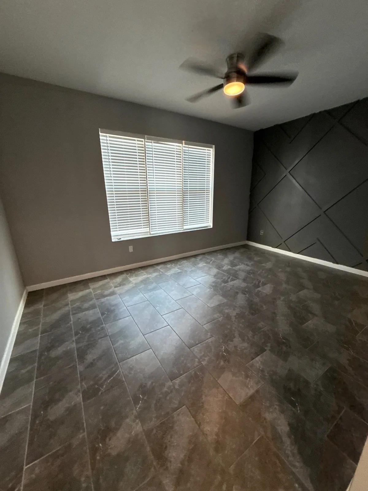 Interior Painting in Port Saint Lucie, Florida. Empty bedroom with grey walls and a dark accent wall with applied geometric trim, ceiling fan and window with blinds.