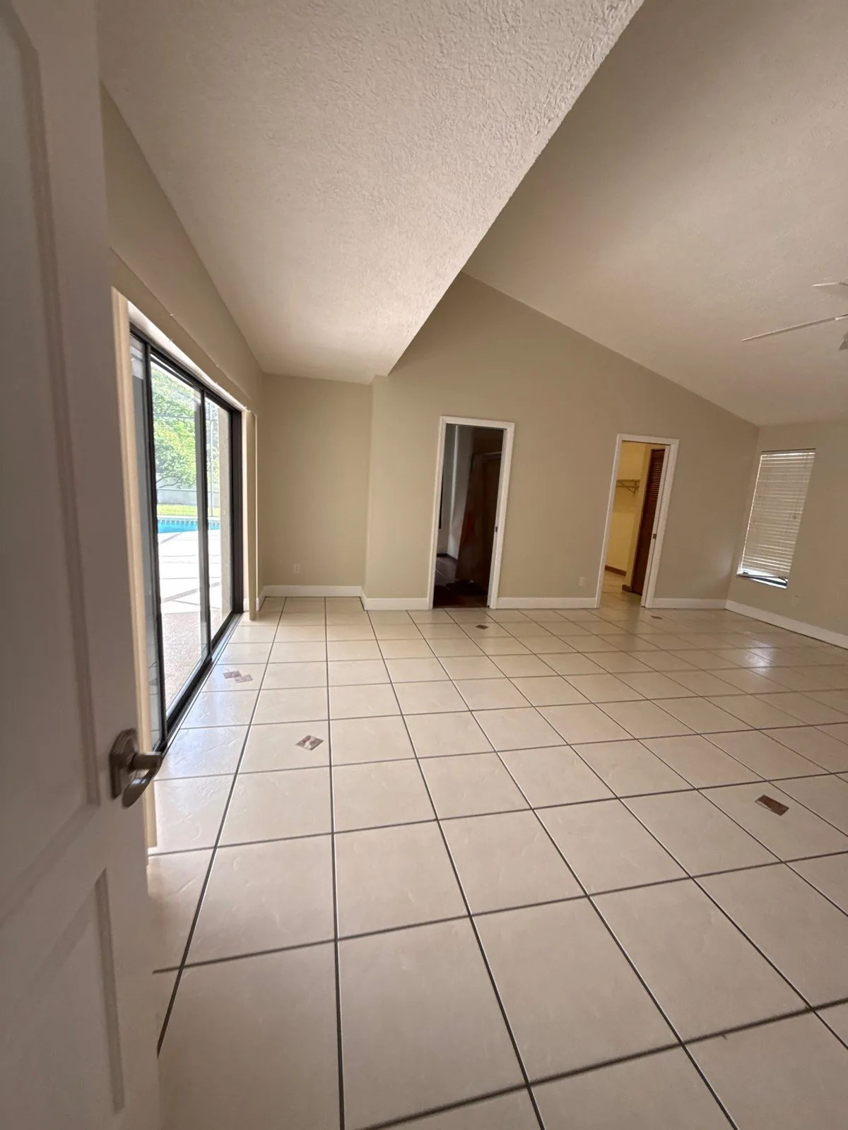 Interior Painting in Port Salerno, Florida. Empty living area with beige walls, vaulted white ceiling, sliding glass door and white tile floor.
