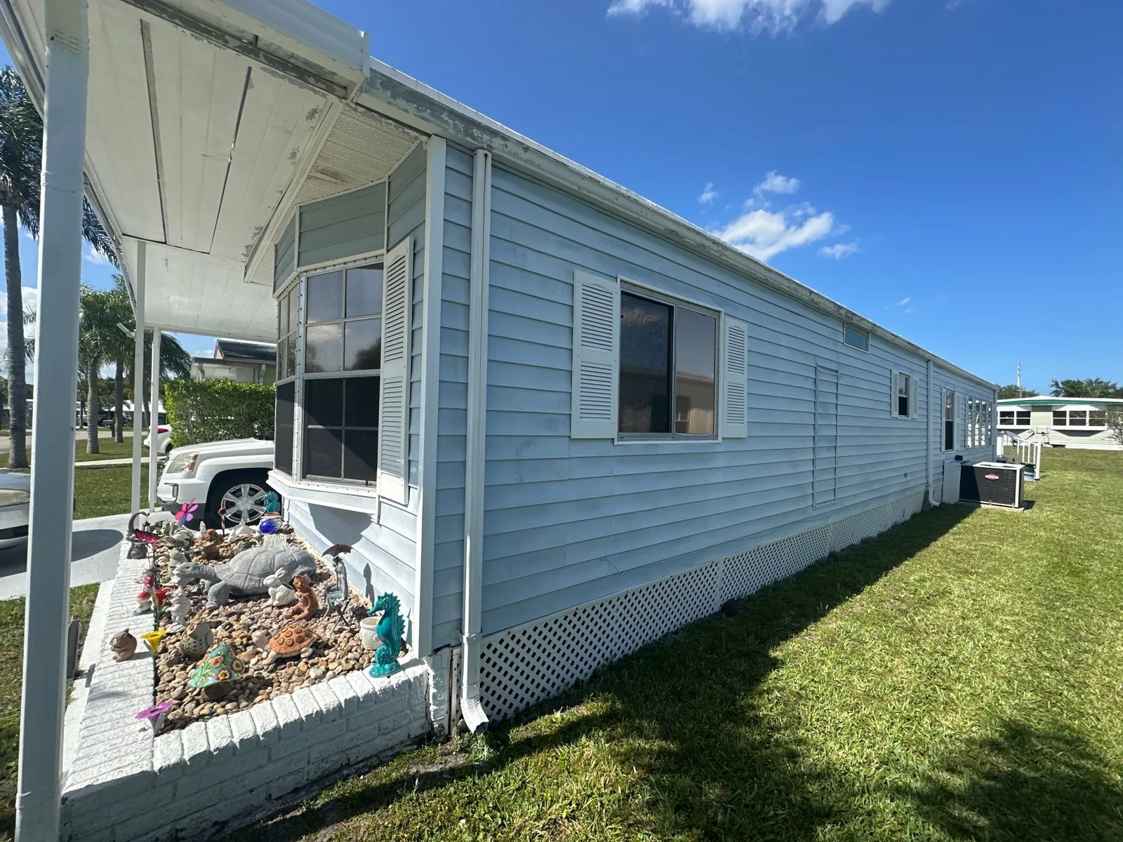 Exterior Painting in River Park, Florida. Single-storey manufactured home with pale blue horizontal siding, white window shutters and white skirting.