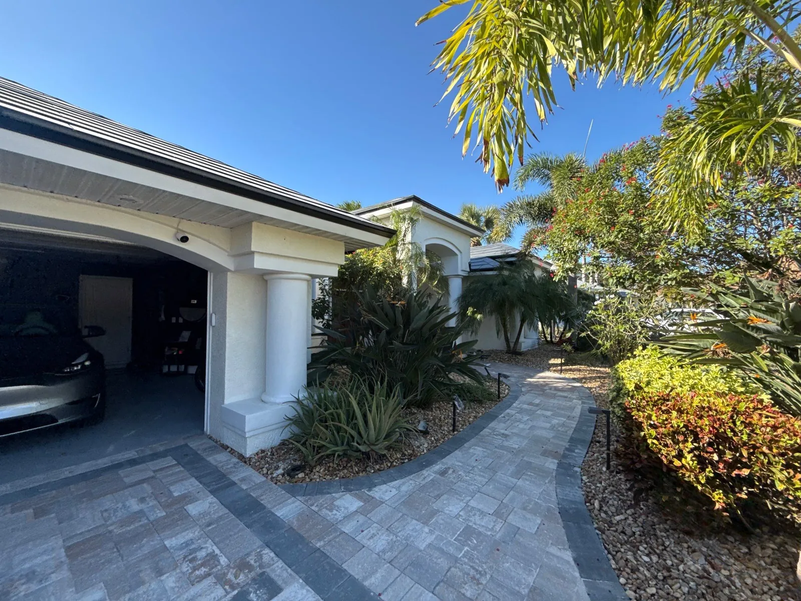 Exterior Painting in Satellite Beach, Florida. Front of a single-storey home with light stucco walls, white columns, paver driveway and tropical landscaping.
