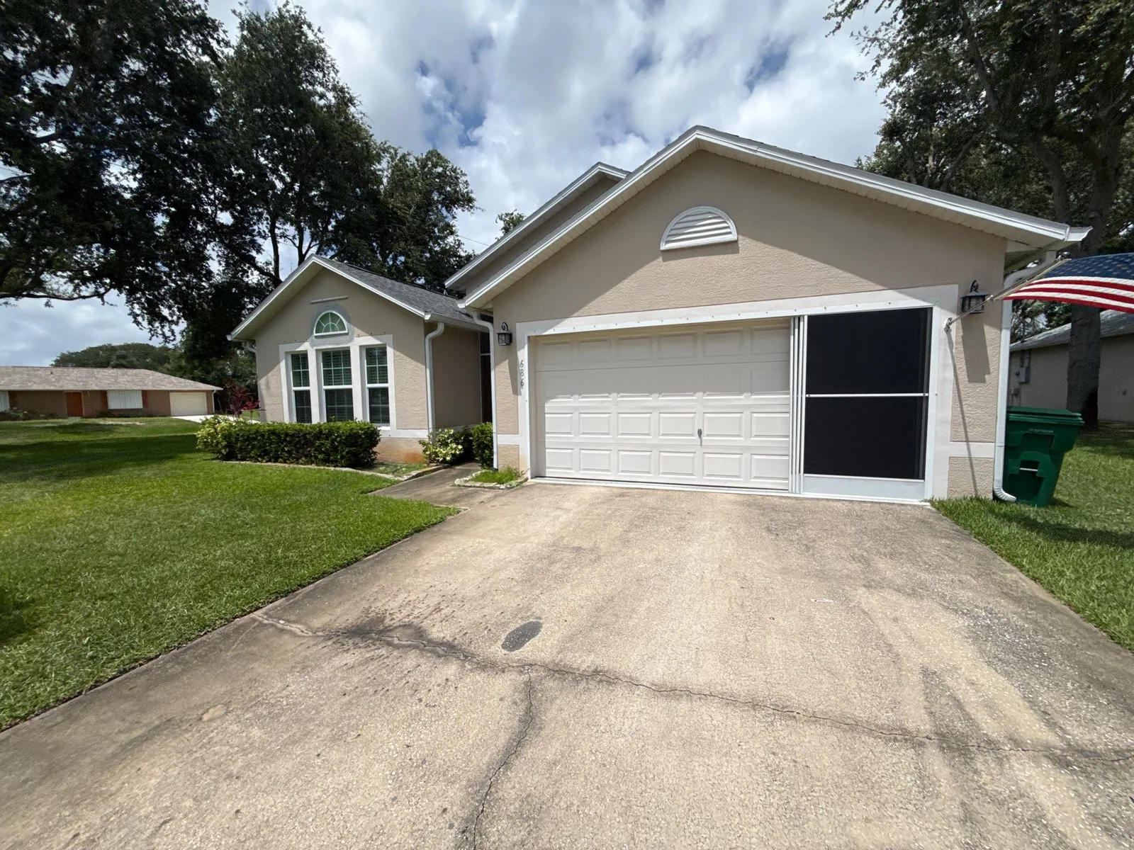 Exterior Painting in Sebastian, Florida. Single-storey stucco house painted tan with white garage door and trim, concrete driveway and front lawn.