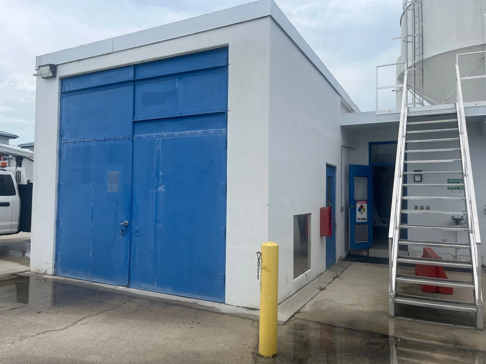 Commercial Painting in Stuart, Florida. White painted concrete utility building with blue roll-up doors and blue entry door, industrial tank behind.