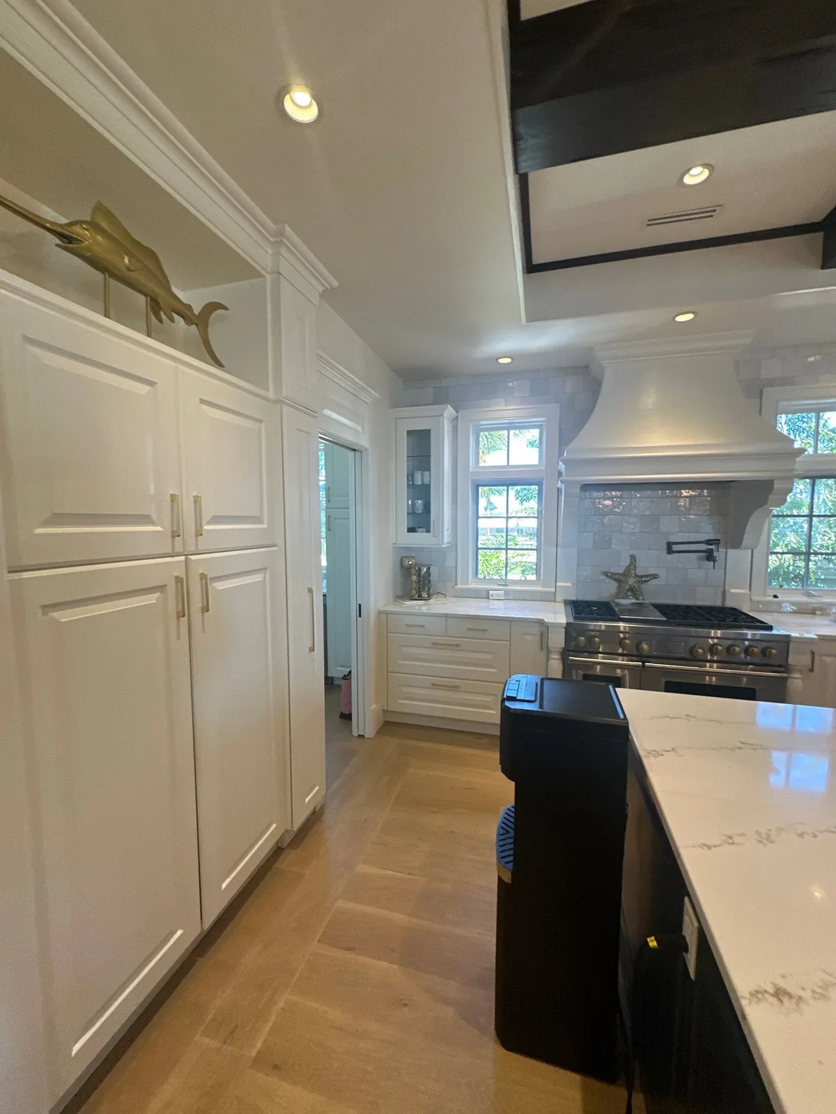 Cabinet Refinishing in Vero Beach, Florida. Kitchen with tall white panel-front cabinets, white range hood and dark island.