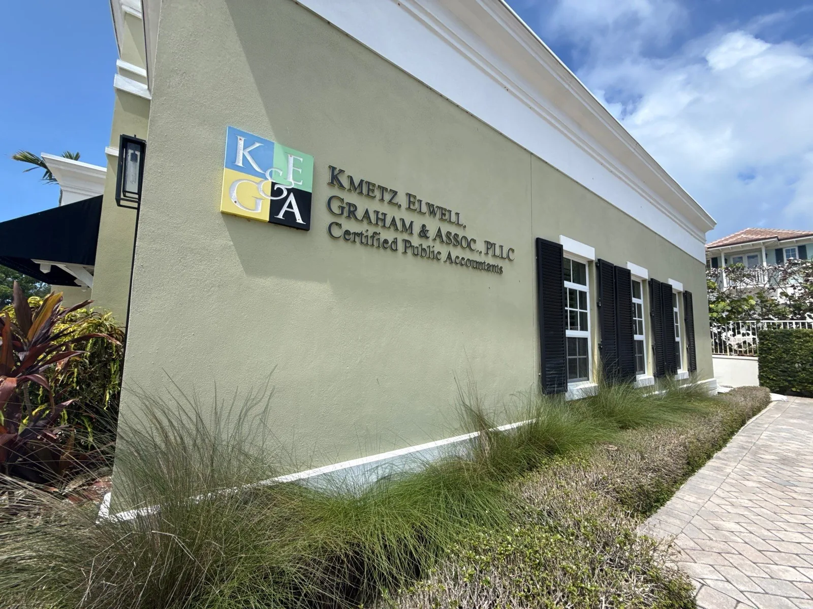 Commercial Painting in Vero Beach, Florida. Single-storey commercial office building exterior, olive-green painted stucco with white trim and dark shutters, mounted business signage and landscaping in front.
