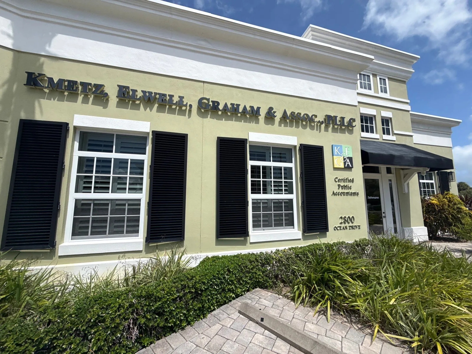 Commercial Painting in Vero Beach, Florida. Commercial office building exterior, olive stucco walls with white trim, black shutters and building signage, viewed from the paver walkway.