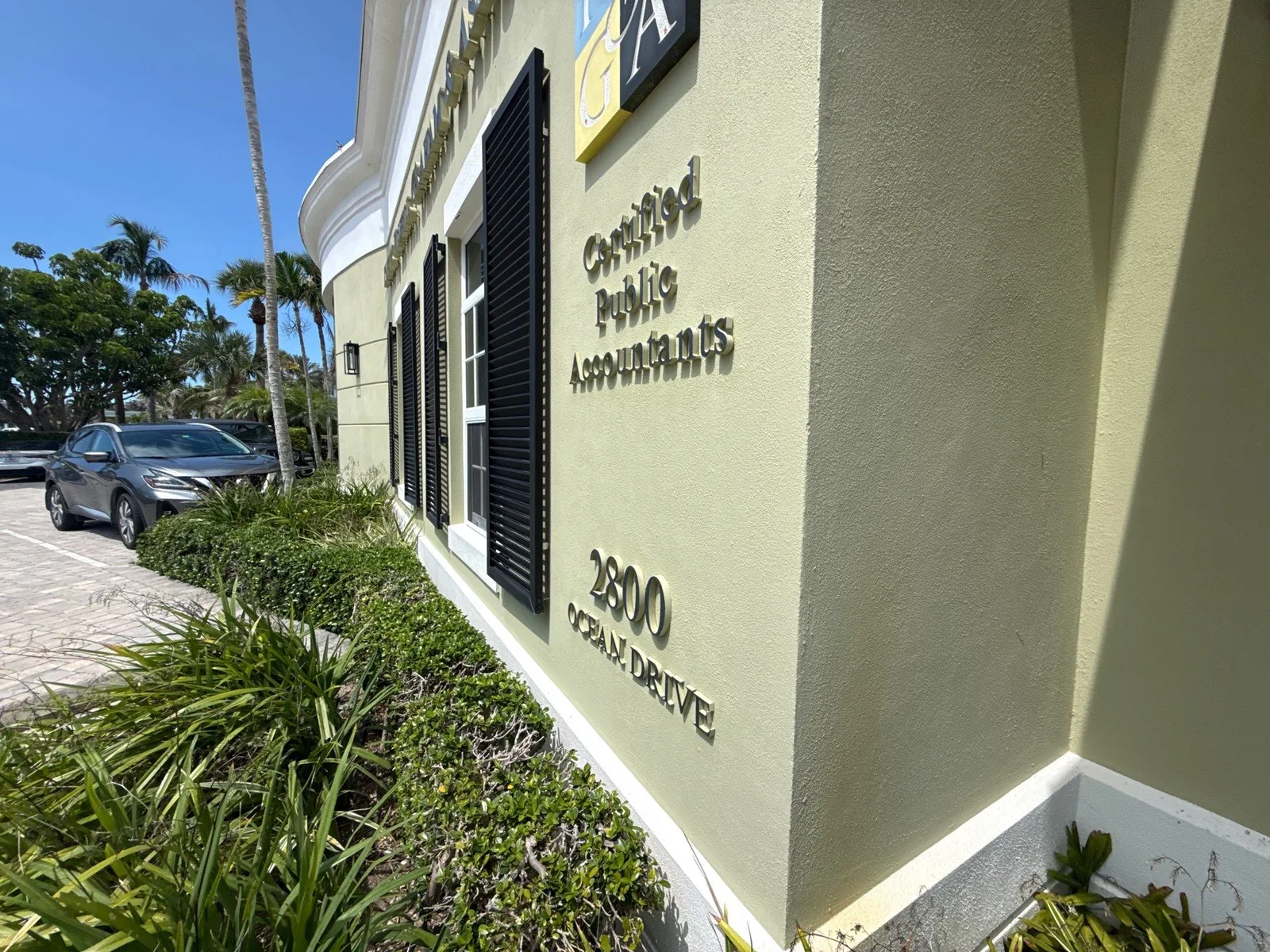 Commercial Painting in Vero Beach, Florida. Corner of a pale yellow stucco office building with white trim, black louvered shutters and raised lettering.