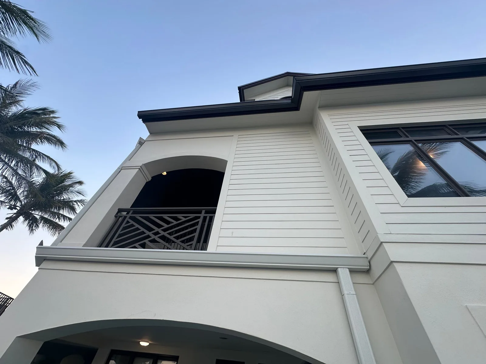 Exterior Painting in Vero Beach, Florida. Upward view of a white lap-siding second storey with dark trim, a covered balcony and decorative railing.