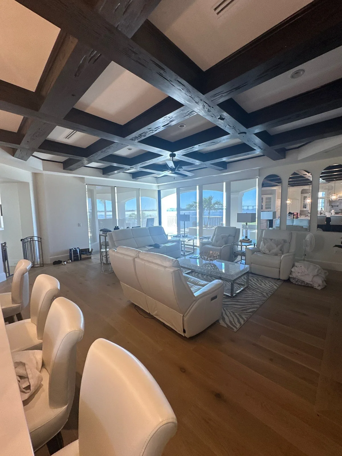Interior Painting in Vero Beach, Florida. Open living room with white coffered ceiling and dark-stained beams, white walls and light wood floor.