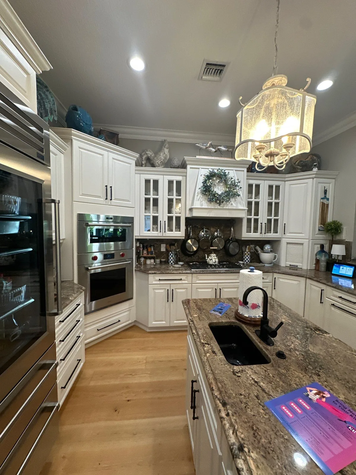 Cabinet Refinishing in Wabasso Beach, Florida. Kitchen with white raised-panel cabinets, glass-front uppers, stone countertops and wood flooring.