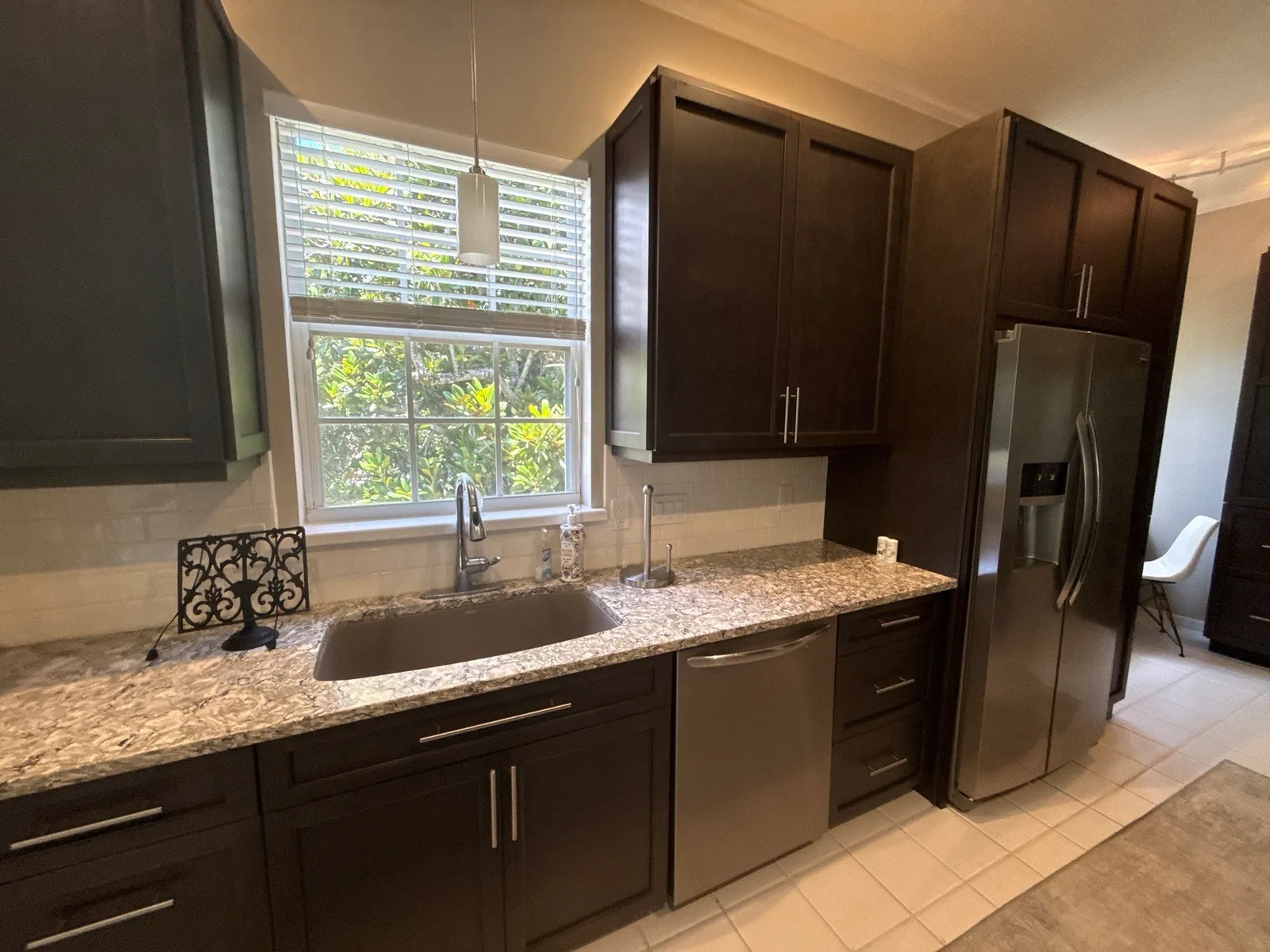 Cabinet Refinishing in Wabasso Beach, Florida. Kitchen with dark espresso cabinets, granite countertops, stainless dishwasher and refrigerator, window above the sink.