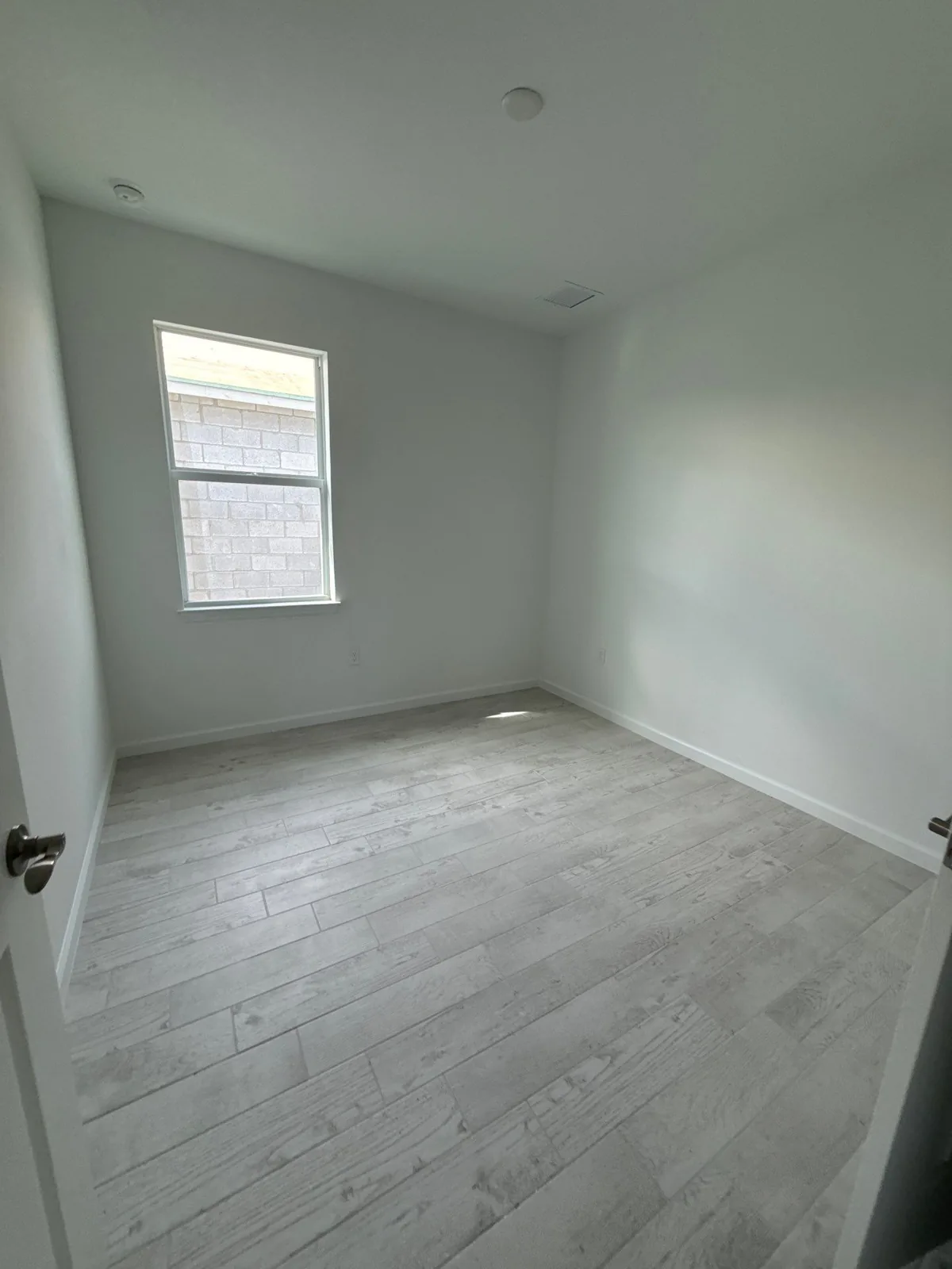 Interior Painting in Wabasso, Florida. Empty bedroom with white walls and ceiling, one window and grey plank flooring.