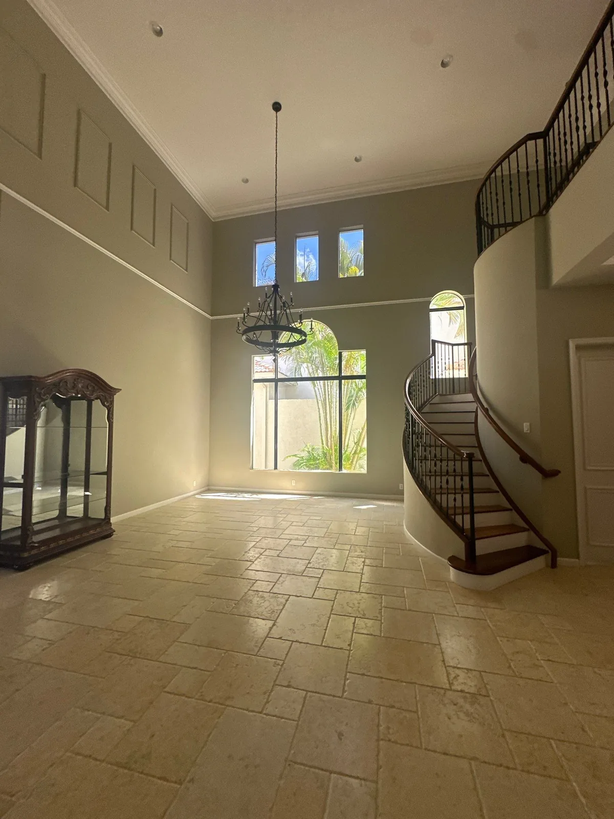 Interior Painting in Whisper Walk, Florida. Double-height great room with tall painted walls, wall panelling, crown moulding, arched window wall and a curved staircase with iron railing.
