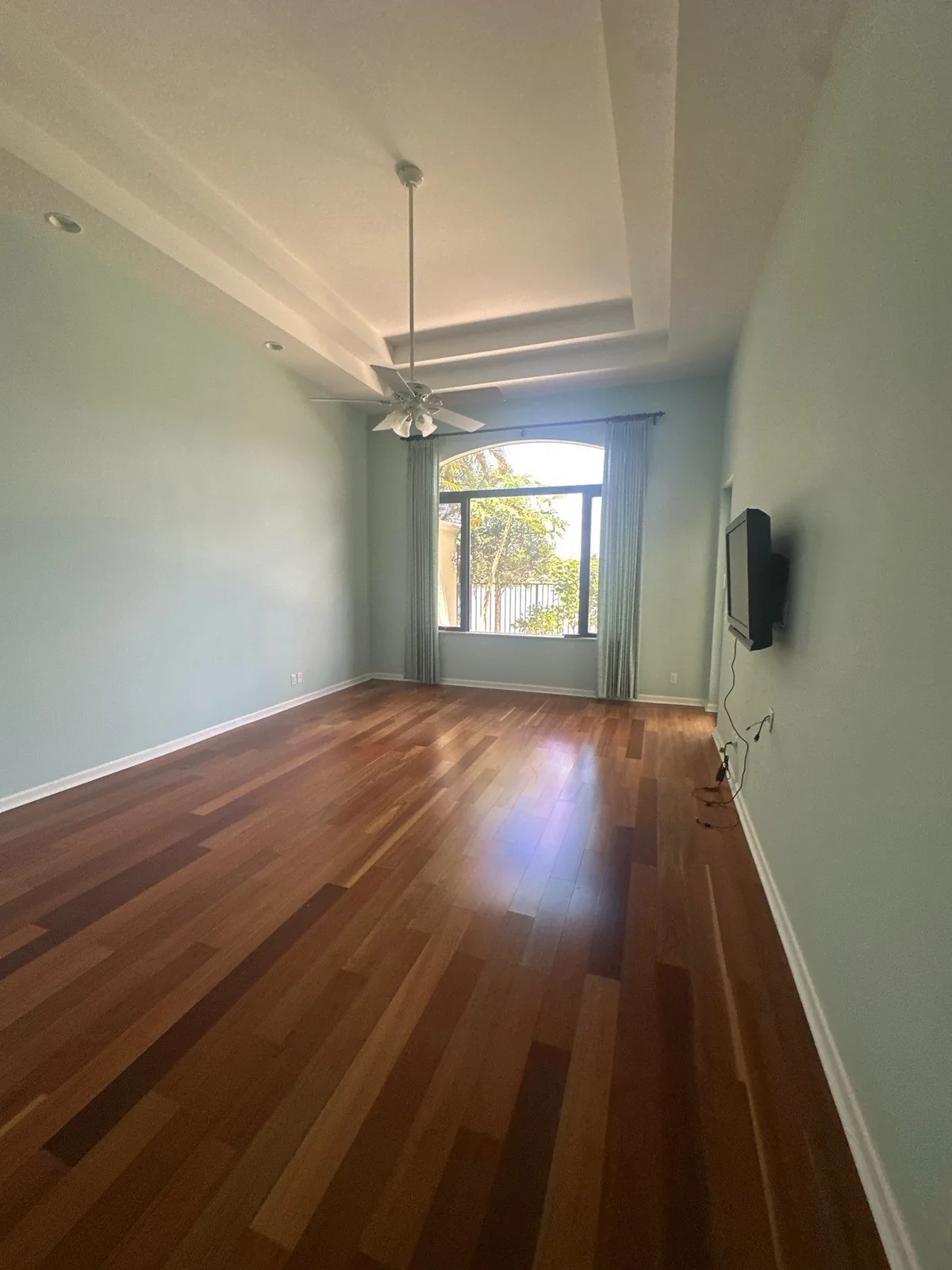 Interior Painting in Whisper Walk, Florida. Empty bedroom with pale green walls, white tray ceiling and ceiling fan above a hardwood floor.